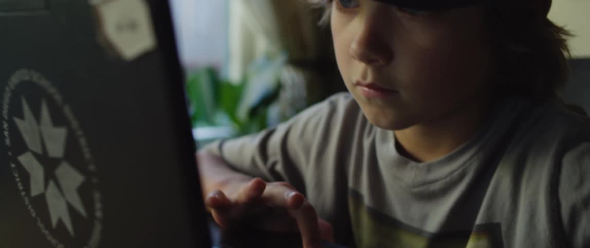 A boy sitting using a laptop at home near a window