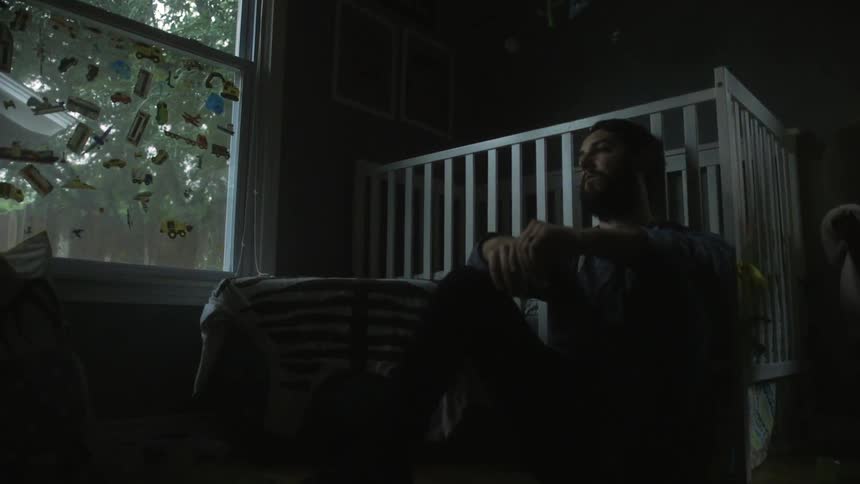 A man is sitting near a crib in a dark room