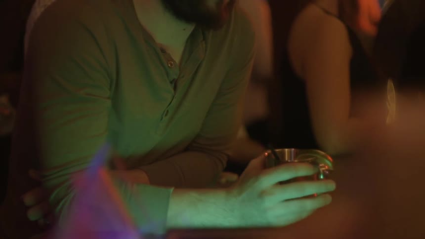 Man looks down at his drink at a crowded nightclub
