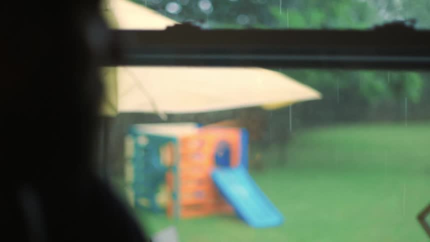 Man looks out a house window while it rains outside