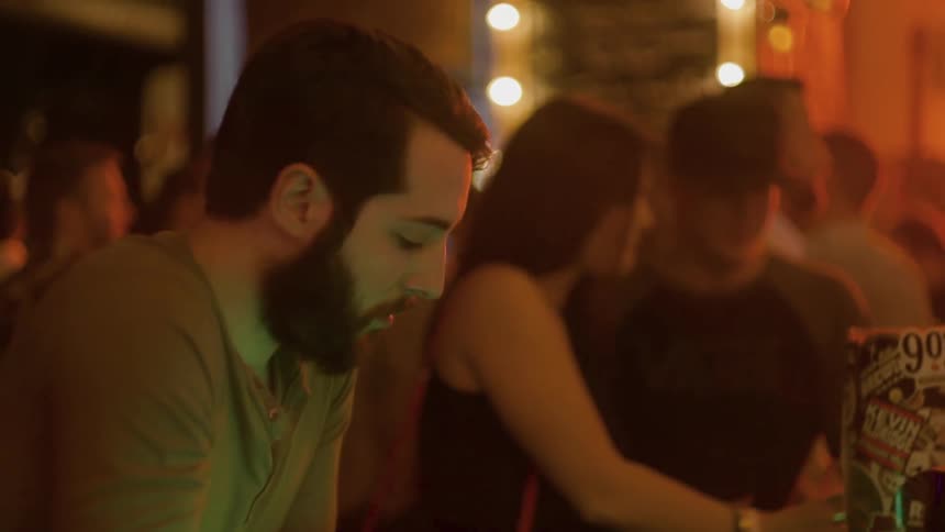 A man is sitting at a bar as others have drinks