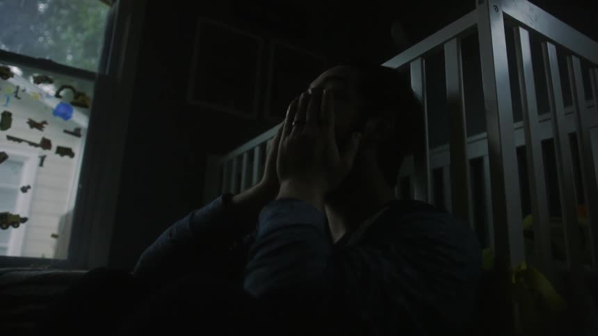 A man sits in a dark room rubbing his face
