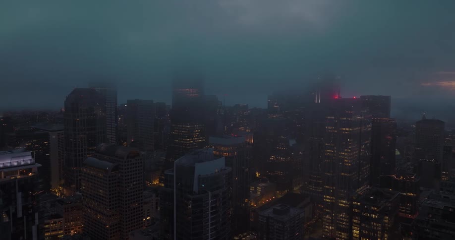 Fog and mist obscure the tops of high rise buildings and skyscapers as night falls