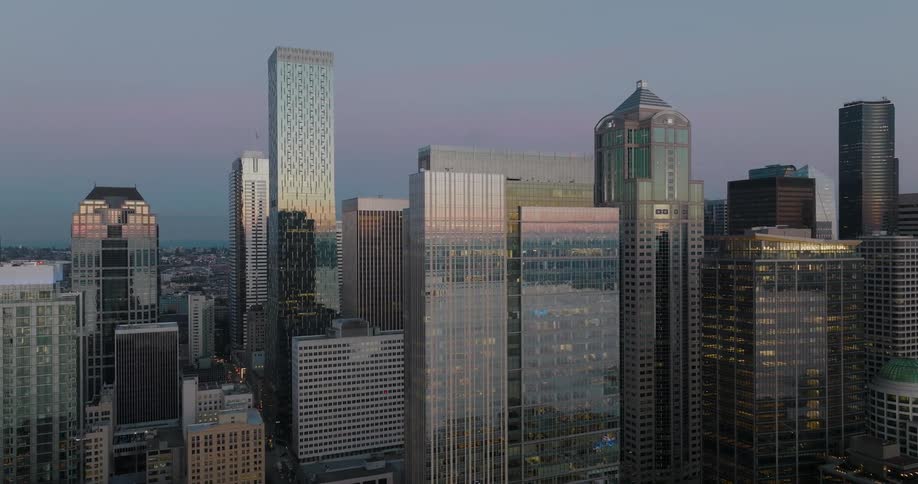 Ascending over downtown buildings as they reflect a painted sky at sunset