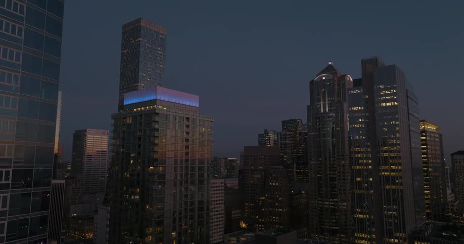 Brightly lit city buildings reflect a golden sky on the horizon