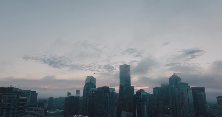 Tilt down from an early morning sky to reveal backlit high rise towers and skyscrapers in a city