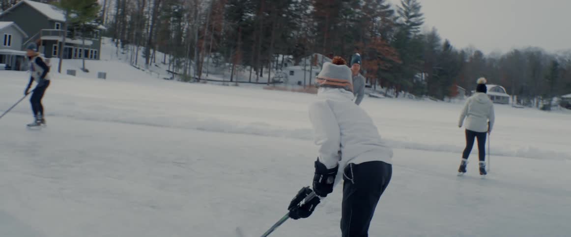 Youths skate across ice outdoors near house practicing hockey
