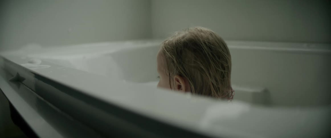 A young girl turns around while sitting in the bathtub