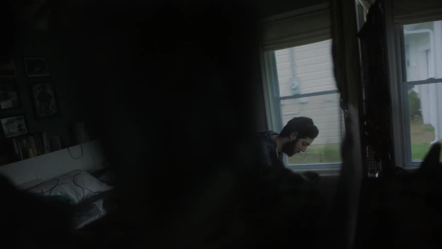 A man is sitting near the window in a dark room