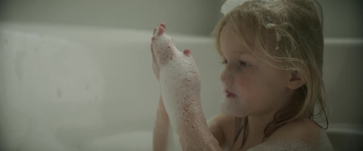 A young child bathing at home puts bubbles on her head