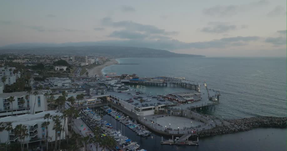 An aerial view of the ocean and boats parked by a dock and cars driving on a street on the coast