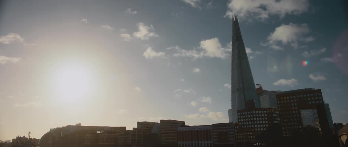 The sun shines brightly above buildings and The Shard building with a few clouds in the sky