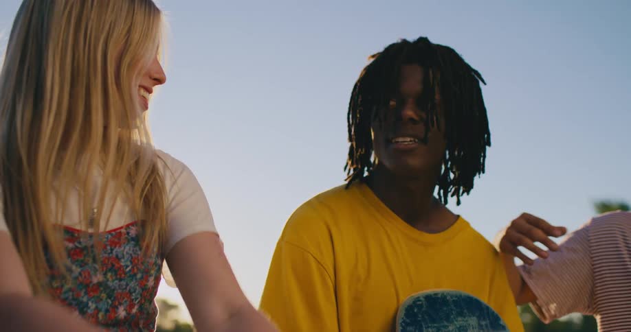 A teenage girl with long blond hair is outside smiling and hanging out with teenage boys