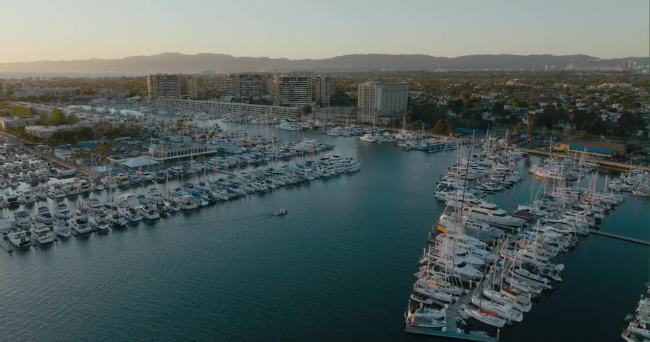 Sun shines through mist from horizon across marina and town stretching to mountains