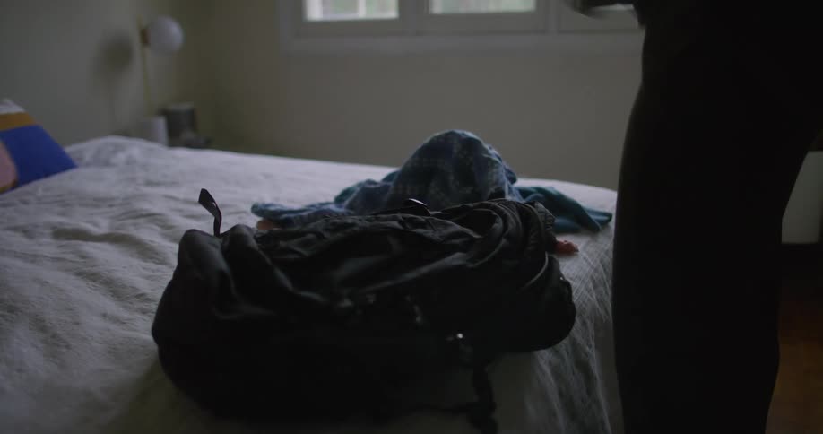 Somebody puts a backpack on a bed next to clothes and they are putting the clothes into the backpack