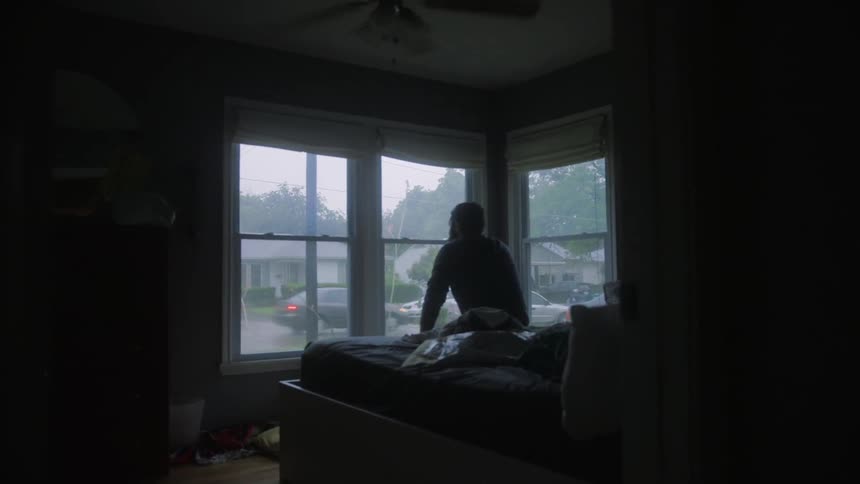 A man sits in front of a window in a dark room
