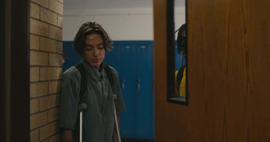 A teenager opens a classroom door for a friend on crutches