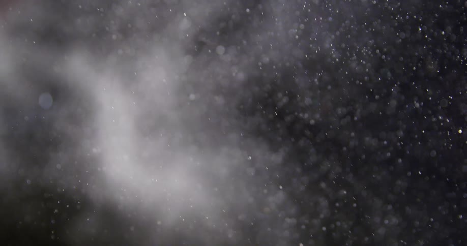 Bubbles and starlike objects move behind white smoke in the darkness