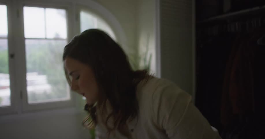A woman in her bedroom takes some clothes out of the closet and folds them