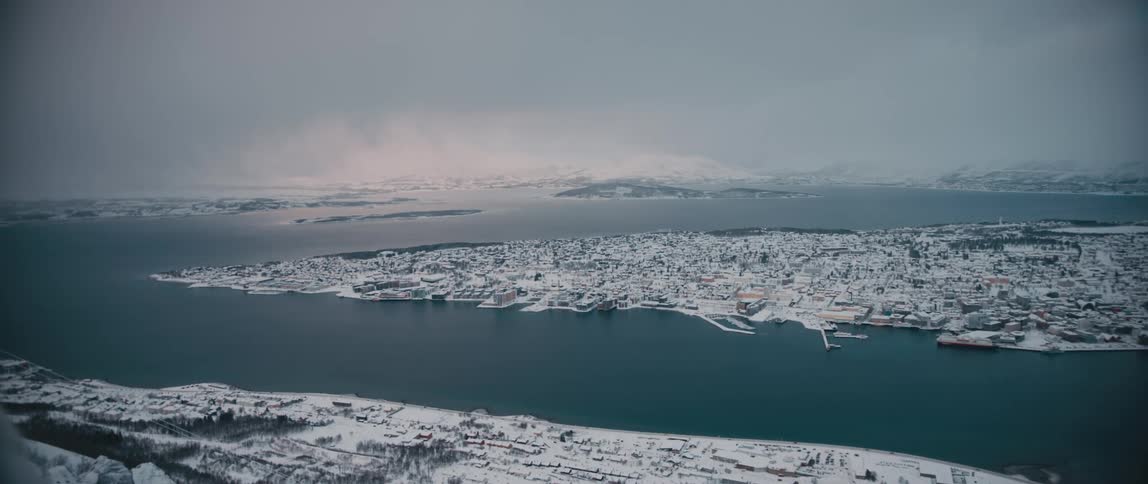 Clouds and mountains on the horizon snowcovered buildings and trees on a peninsula surrounded by still blue water