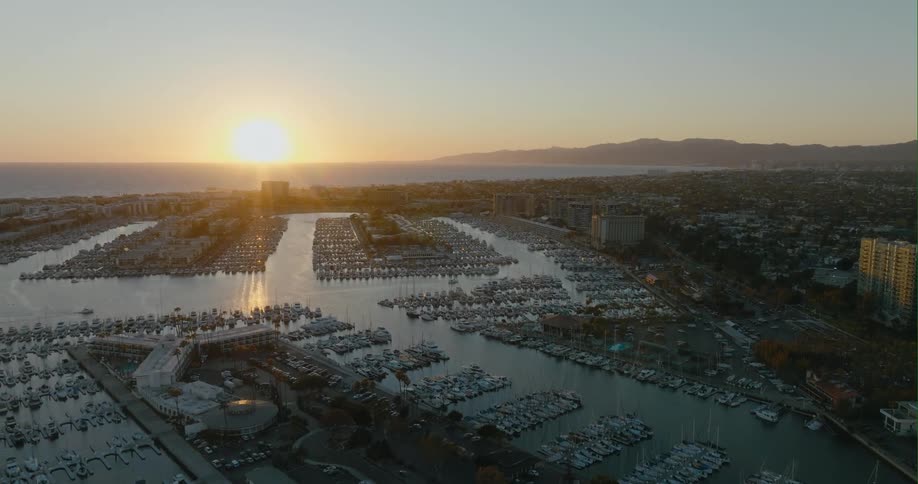Aerial view of boats in a marina along the channel and the sun shining brightly over mountains