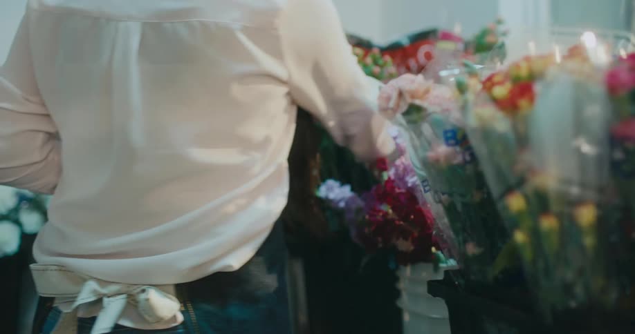 A florist walks around her shop looking at bouquets