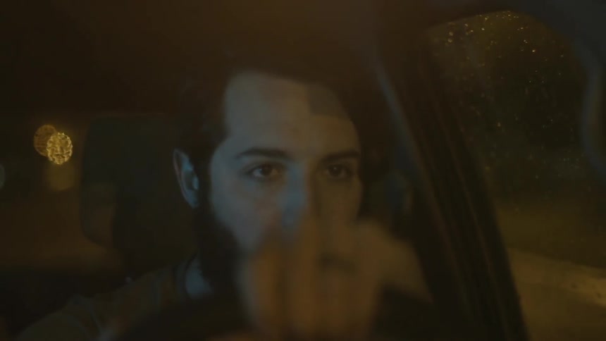 A man is driving a car at night then wipes his face