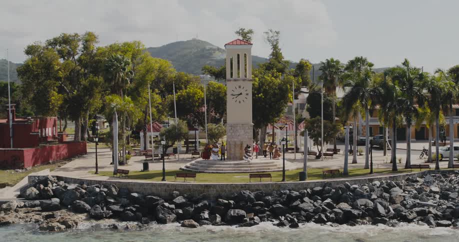 People stand on steps below a clock tower in a park