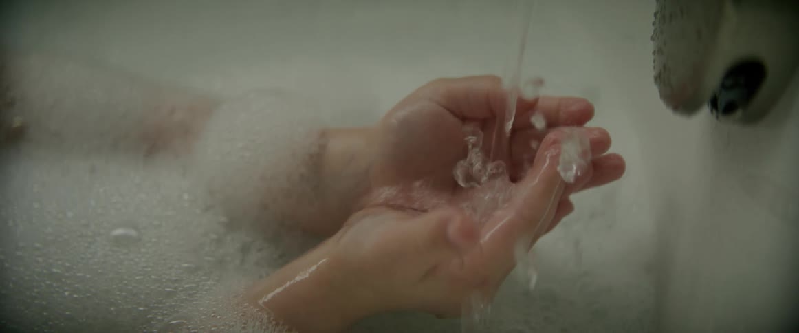 A child holding their hands under a running faucet while taking a bubble bath