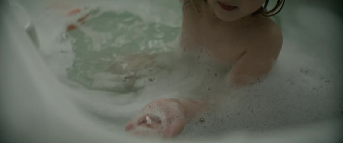 Child plays with foam while sitting in tub bathing