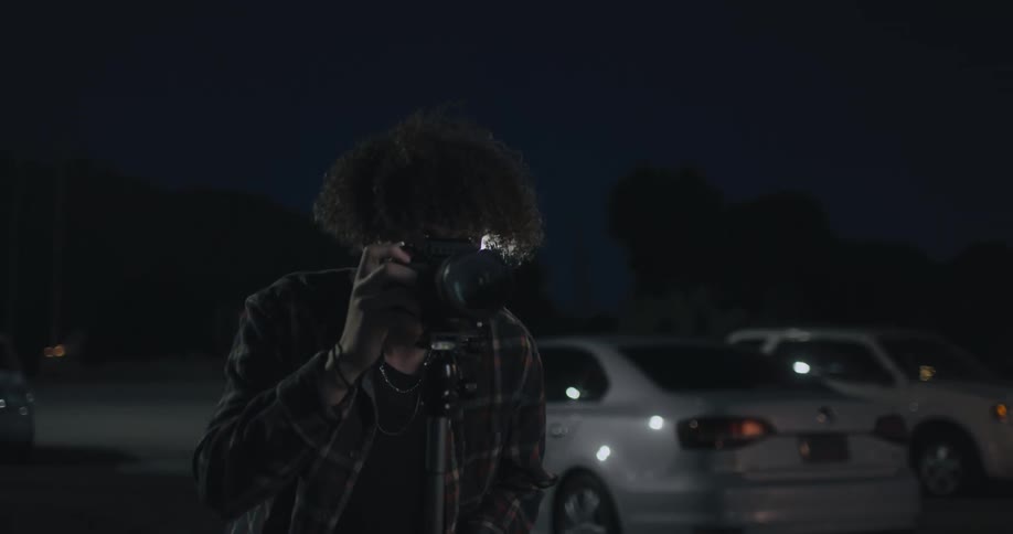 A man is outdoors and taking pictures with a camera at night