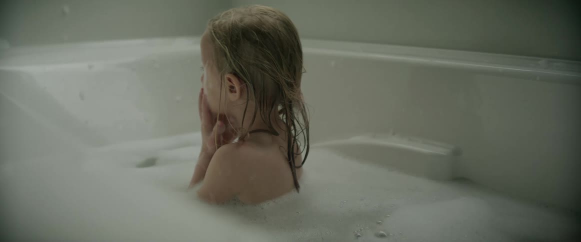 A girl sitting in a bath tub washing her face with the suds