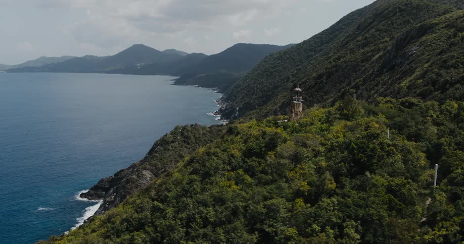 A tower atop a forested mountain ridge on the coast during the day
