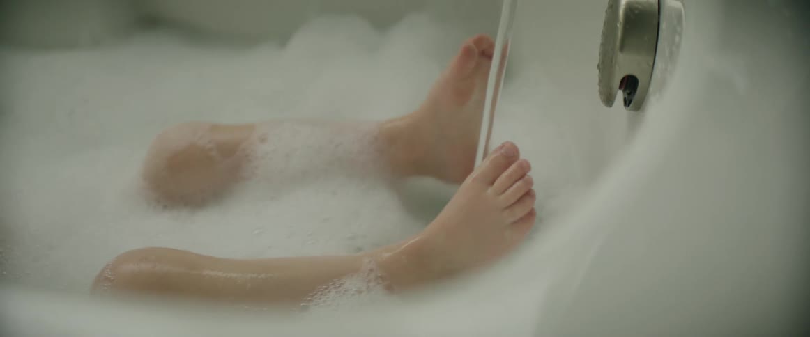 A child holding their feet under a running faucet while taking a bubble bath