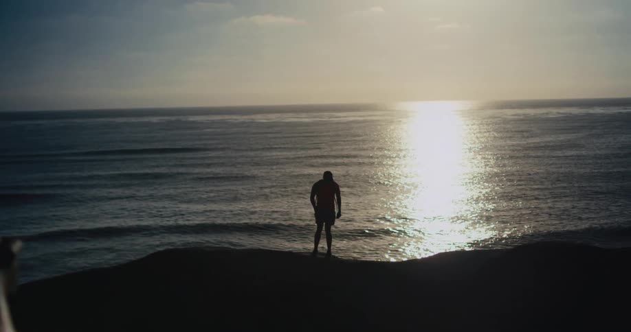 A man is walking on the coast of a beach at dusk
