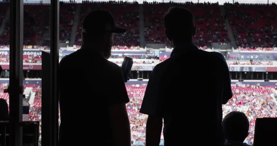 Two men tap their beer cans together at a sporting event