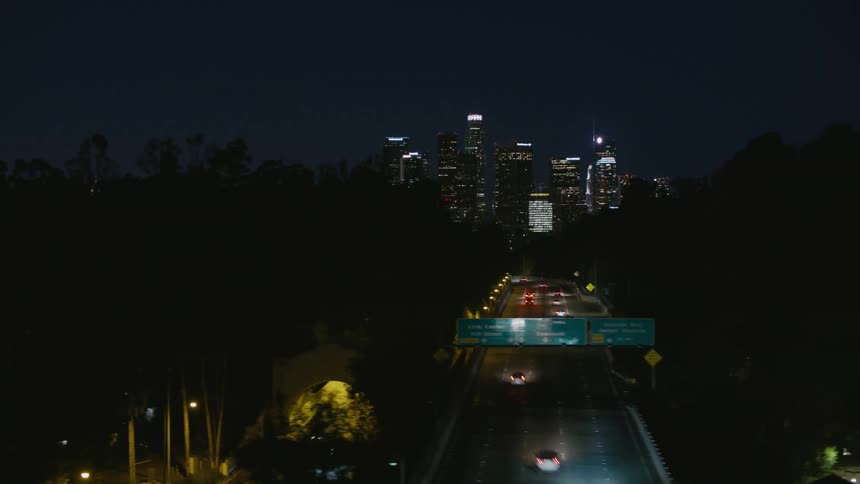 Cars travel on the busy highway heading towards the city buildings at night