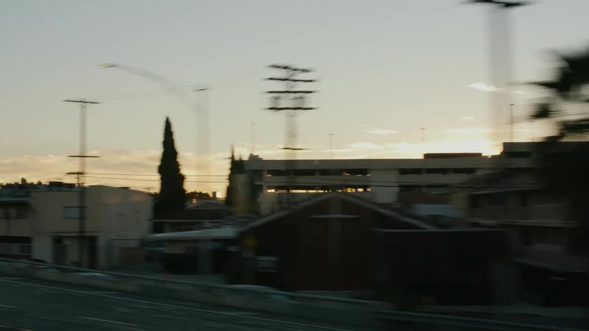 Traveling past buildings and trees in a small city at sunset