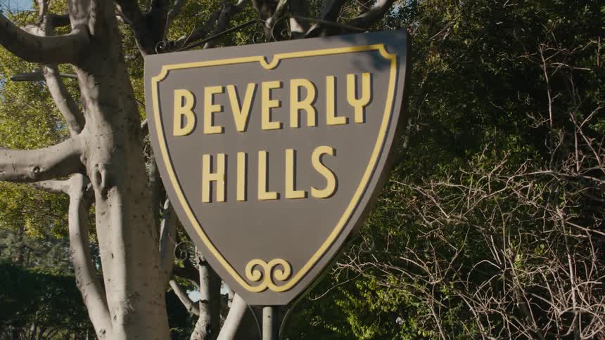 The sun is shining on a sign near trees saying beverly hills