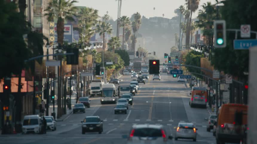 A scene of vehicles moving along street past businesses and toward a fog covered hill comes into focus