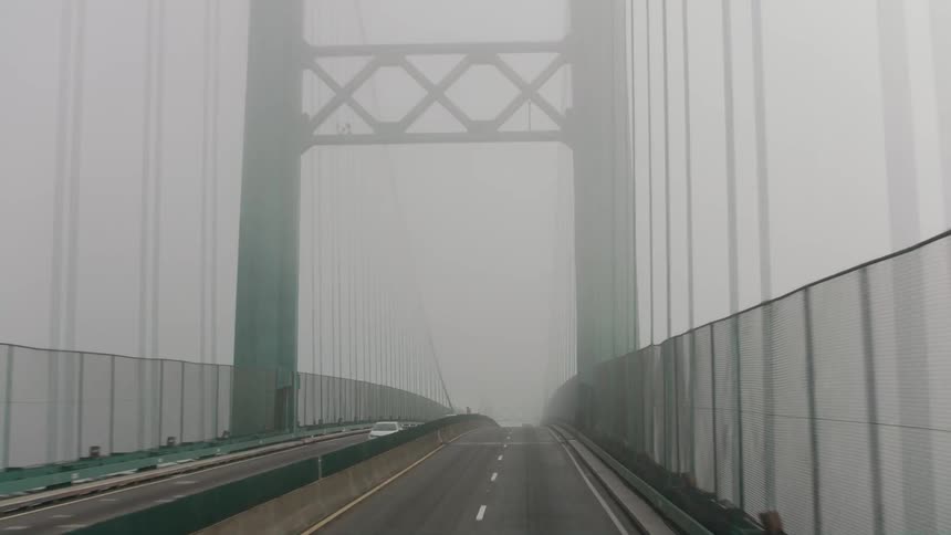Traffic moves across a bridge through the fog