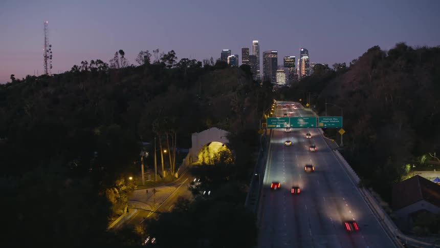 Aerial of cars commuting on freeway at night with skyline in the distance
