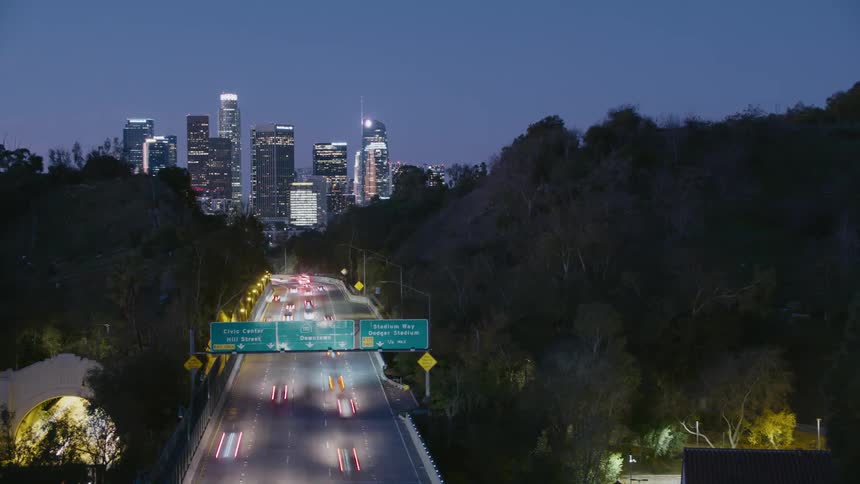 Timelapse of traffic speeding along control access highway leading toward city skyline at night