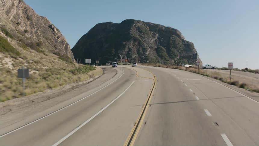 Traffic flows along highway through hills passing a parking lot
