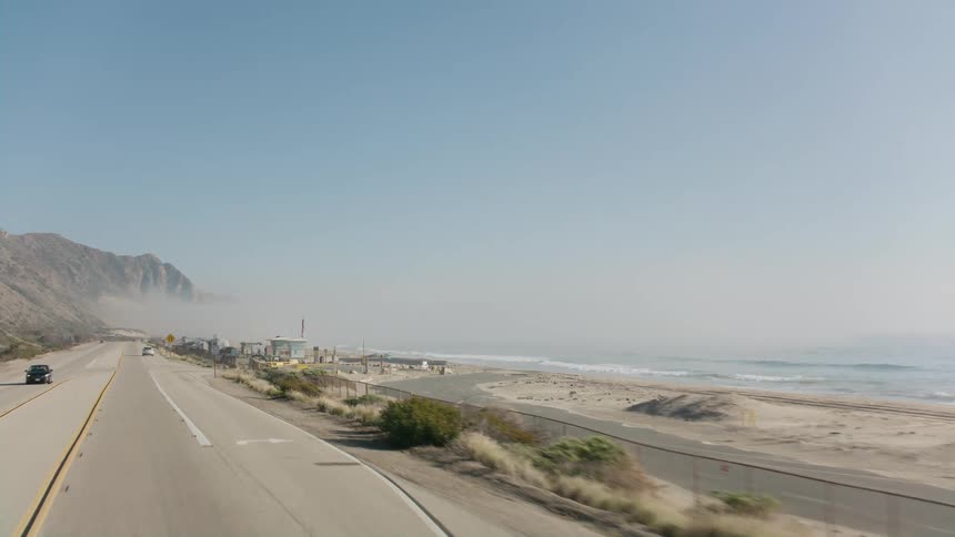 Vehicles speed down a highway along the coast and beach