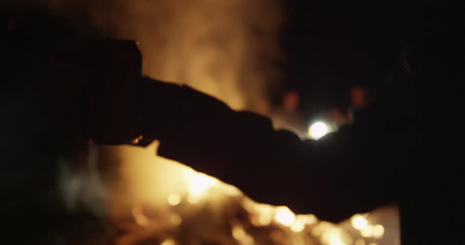 A person holding a can dances in front of a bonfire