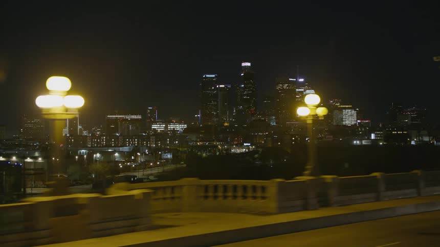 Illuminated city skyscrapers seen from car crossing bridge at night