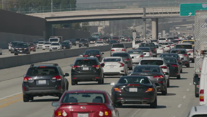 Vehicles sit in bumper to bumper traffic on a multi lane highway near a city