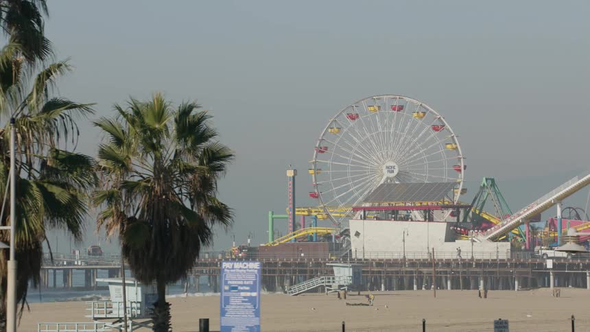 People line a crowded boardwalk at an amusement park along the coast