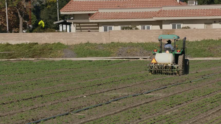 A farmer rides a tractor through a field of crops